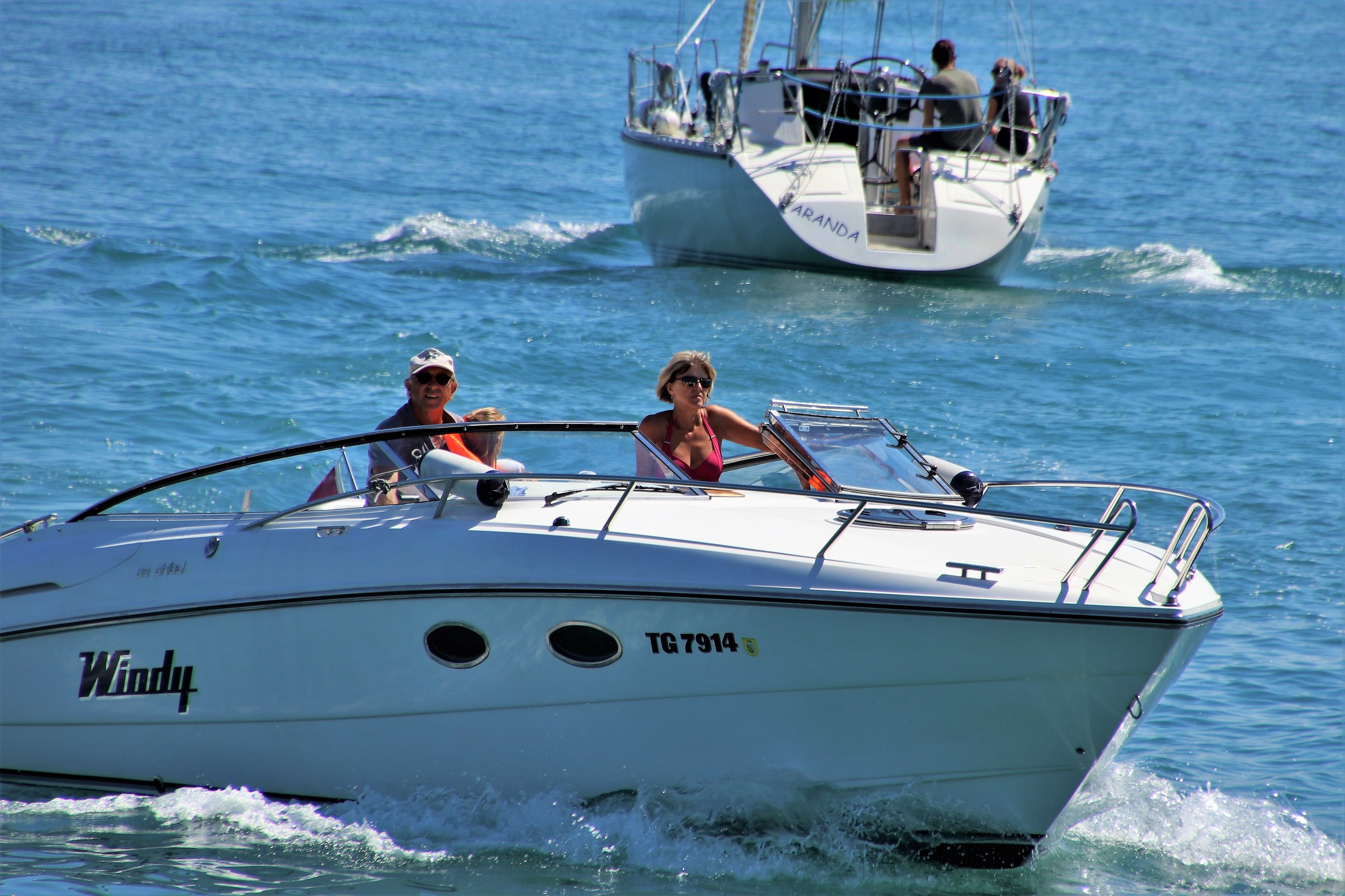 Voilier et speedboat blanc sur mer bleue, trois personnes à bord, planche de bord et fenestrons, coque Windy TG7914 en premier plan. Voilier et speedboat blanc sur mer bleue, trois personnes à bord, planche de bord et fenestrons, coque Windy TG7914 en premier plan.