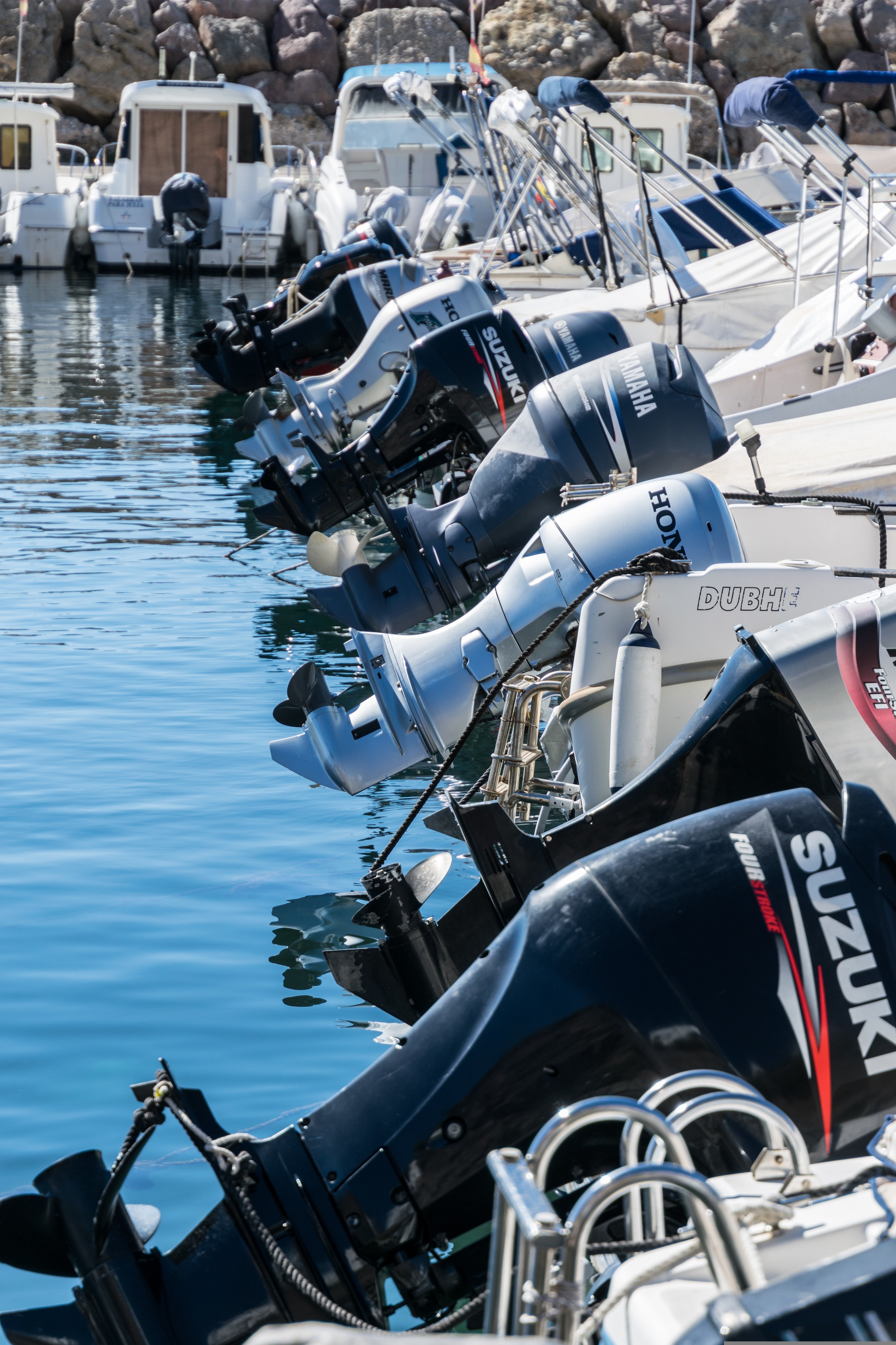 Rangée de bateaux à moteur dans un port, moteurs hors-bord Suzuki et Yamaha inclinés vers l’eau, réflexion sur l’eau bleue. Rangée de bateaux à moteur dans un port, moteurs hors-bord Suzuki et Yamaha inclinés vers l’eau, réflexion sur l’eau bleue.