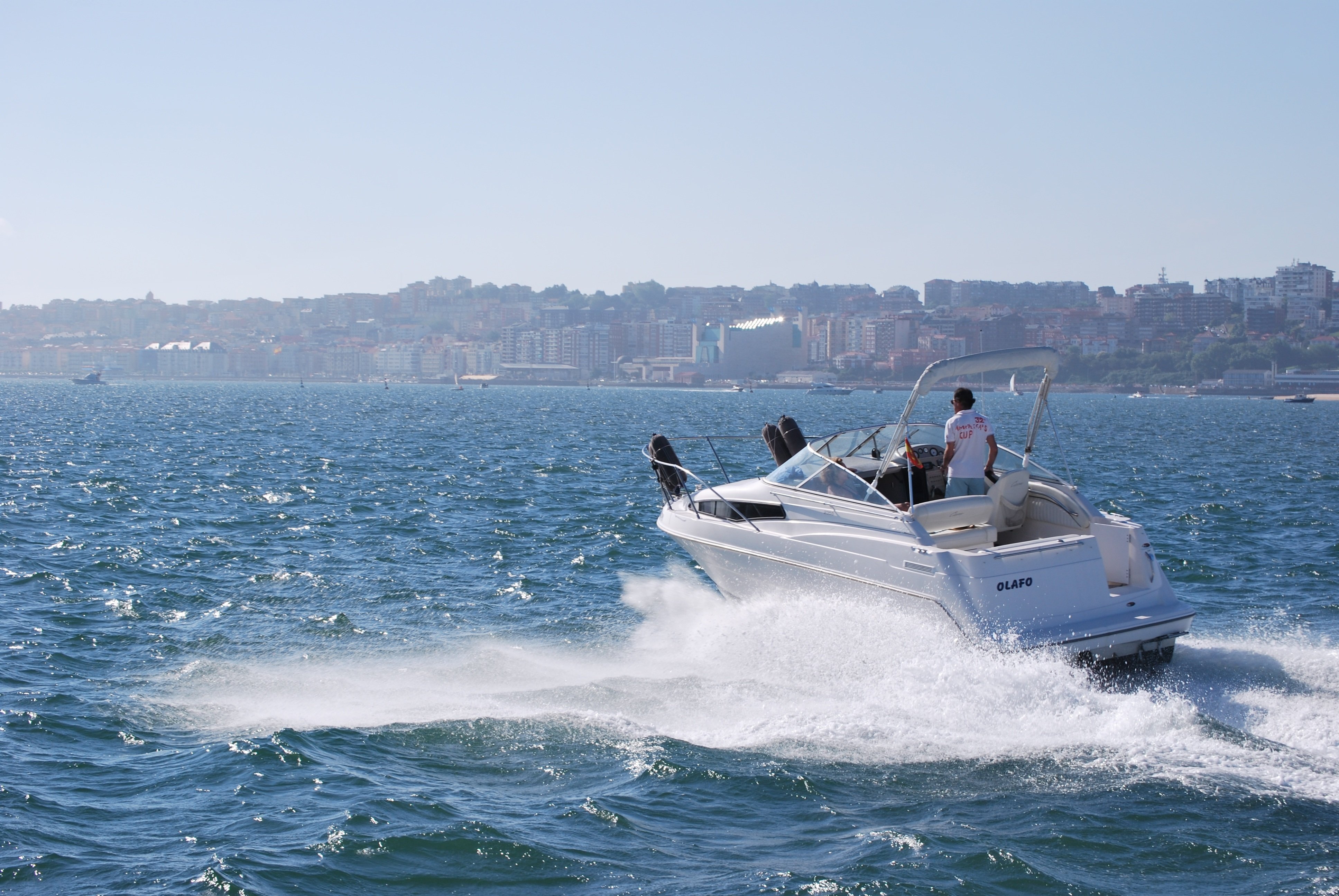 Bateau rapide blanc à motorisation en mer, crique en arrière-plan et ville au rivage sous ciel clair. Bateau rapide blanc à motorisation en mer, crique en arrière-plan et ville au rivage sous ciel clair.